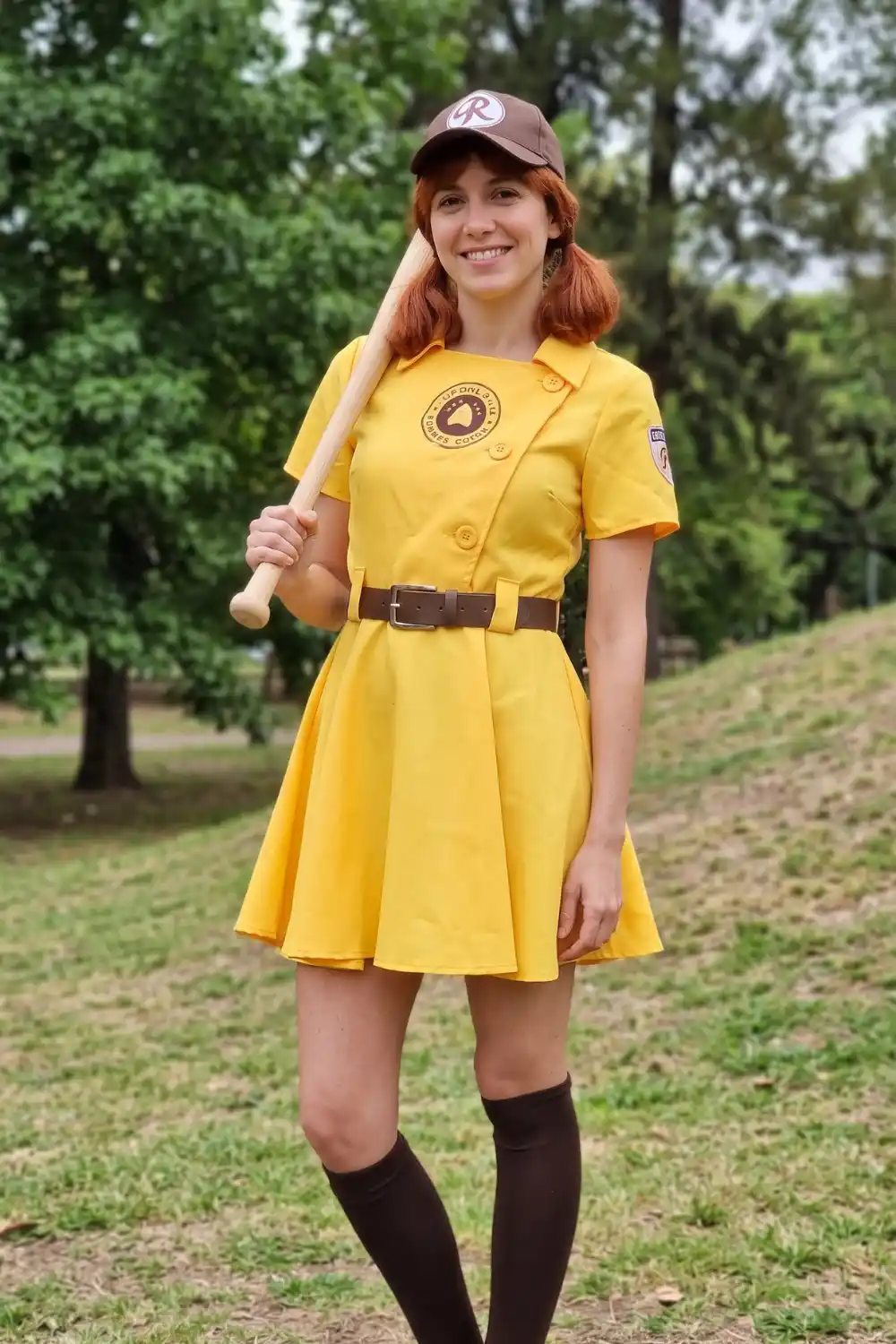 Woman dressed as Rockford Peaches player in yellow uniform with baseball bat and brown cap