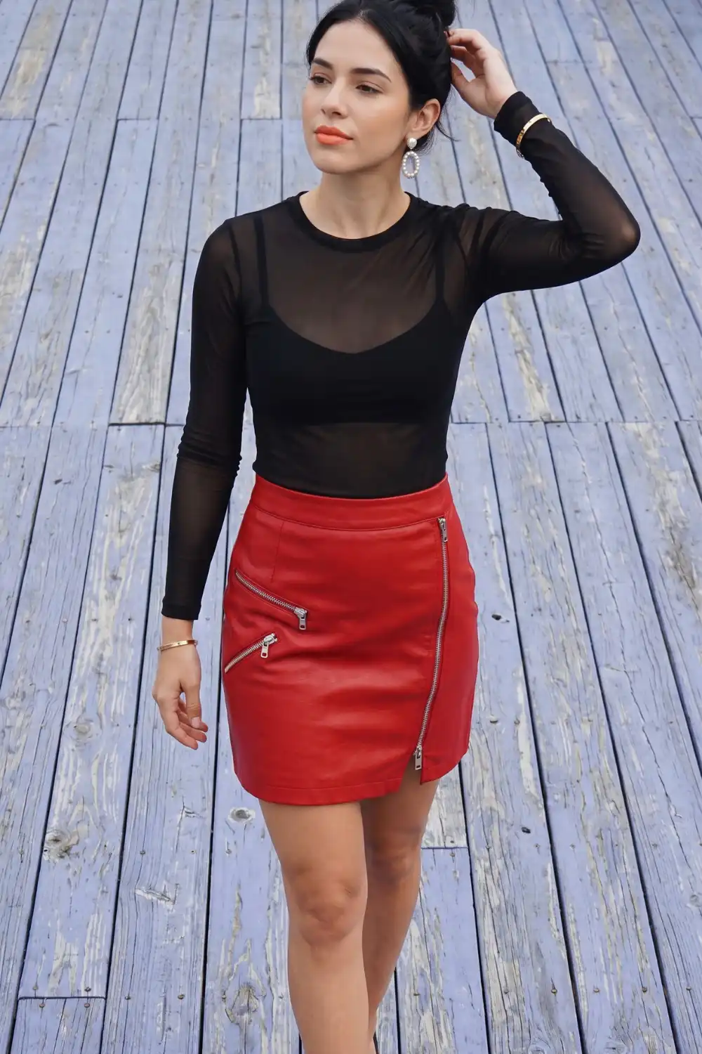 Woman in black sheer mesh long sleeve top with red leather zip detail mini skirt