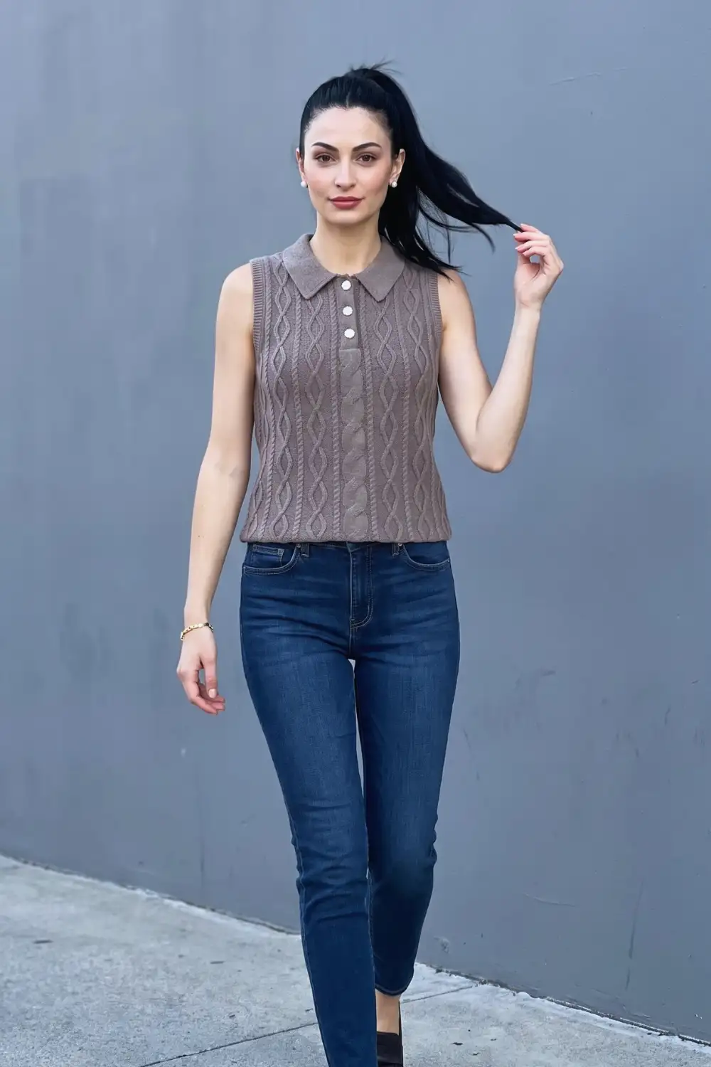 Woman in taupe brown cable knit collared polo sweater vest with dark blue skinny jeans