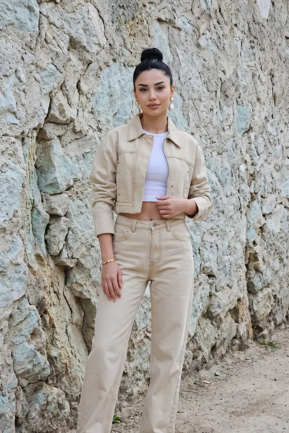 Woman in beige cropped denim jacket with white crop top and beige wide leg jeans
