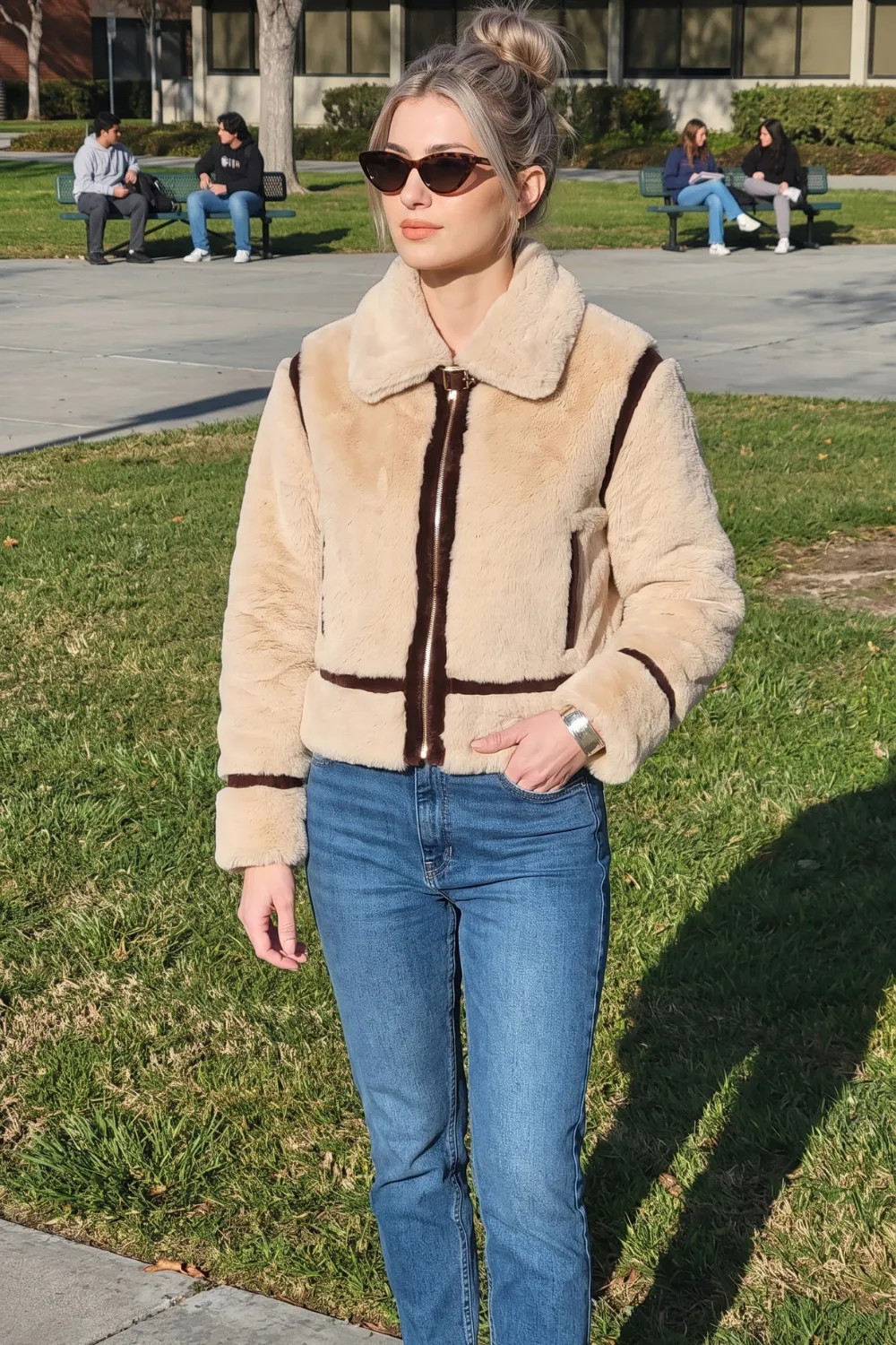 Woman in beige faux fur zip cropped jacket with brown stripe trim and blue straight jeans