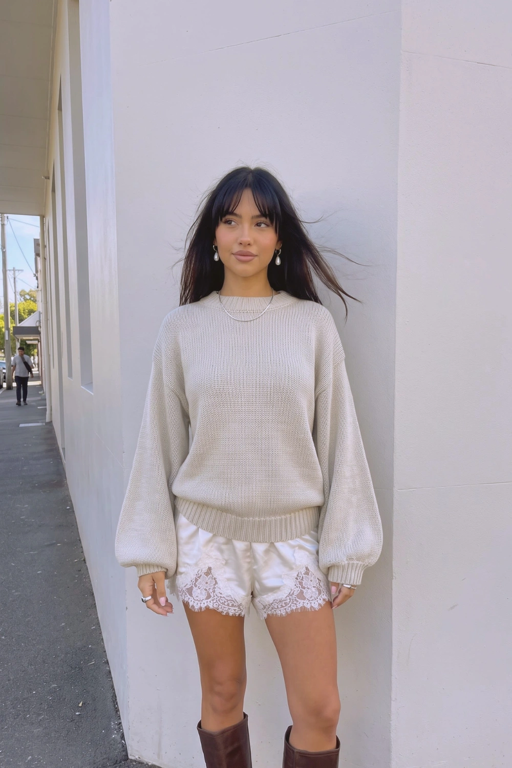 Woman in beige oversized balloon sleeve knit sweater with cream satin lace trim shorts and dark brown knee high boots