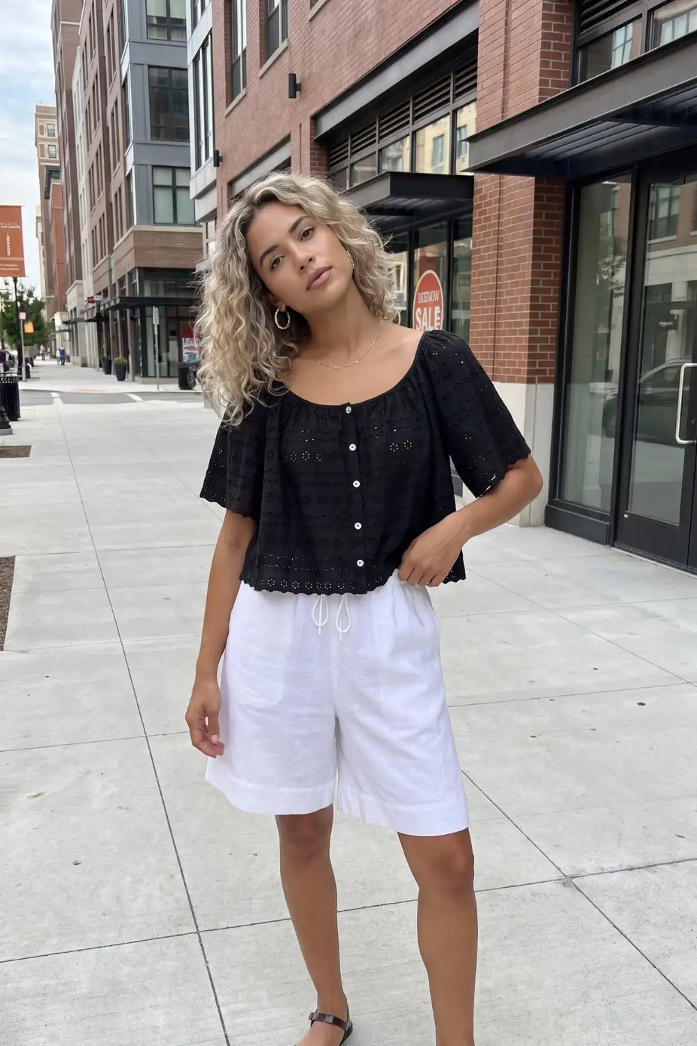 Woman in black eyelet lace crop top with white linen bermuda shorts