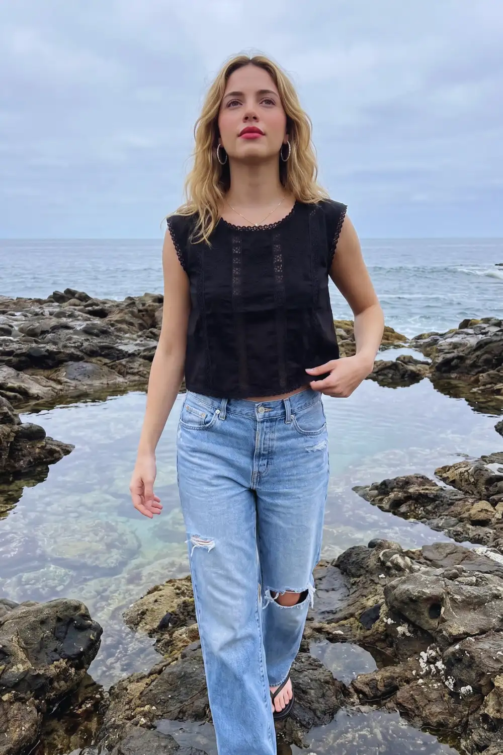 Woman in black eyelet lace sleeveless crop top with light wash distressed wide leg jeans