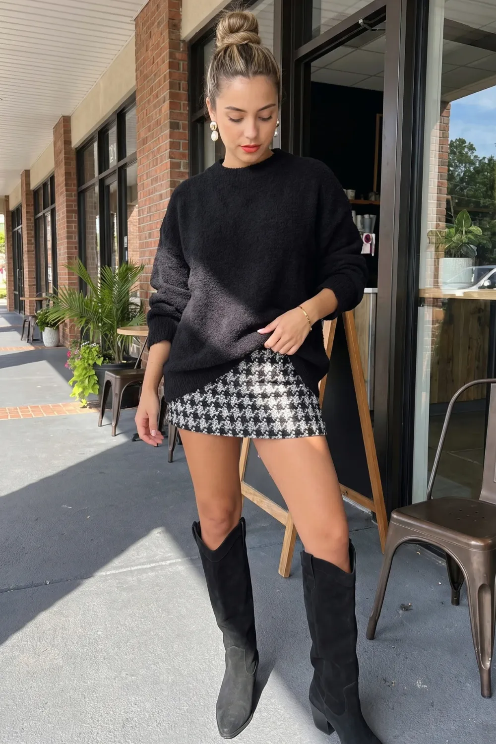 Woman in black oversized knit sweater with black white houndstooth sequin mini skirt and black knee high boots