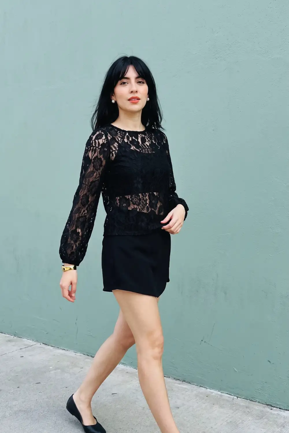 Woman in black sheer floral lace puff sleeve top with black mini skirt and black flats