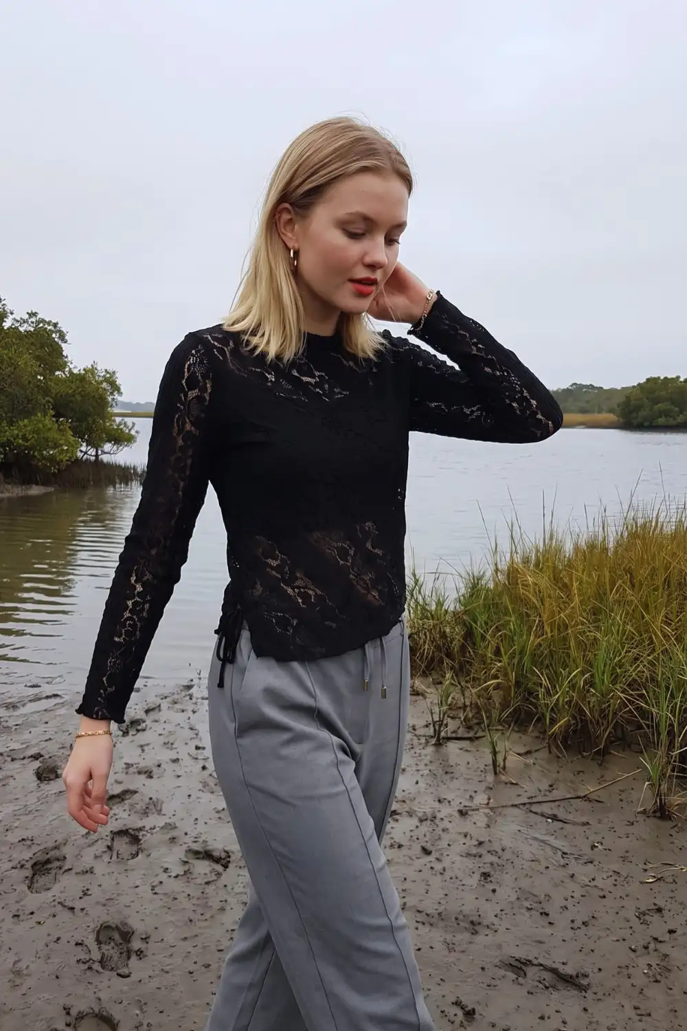 Woman in black sheer lace mock neck ruched side top with light grey wide leg trousers