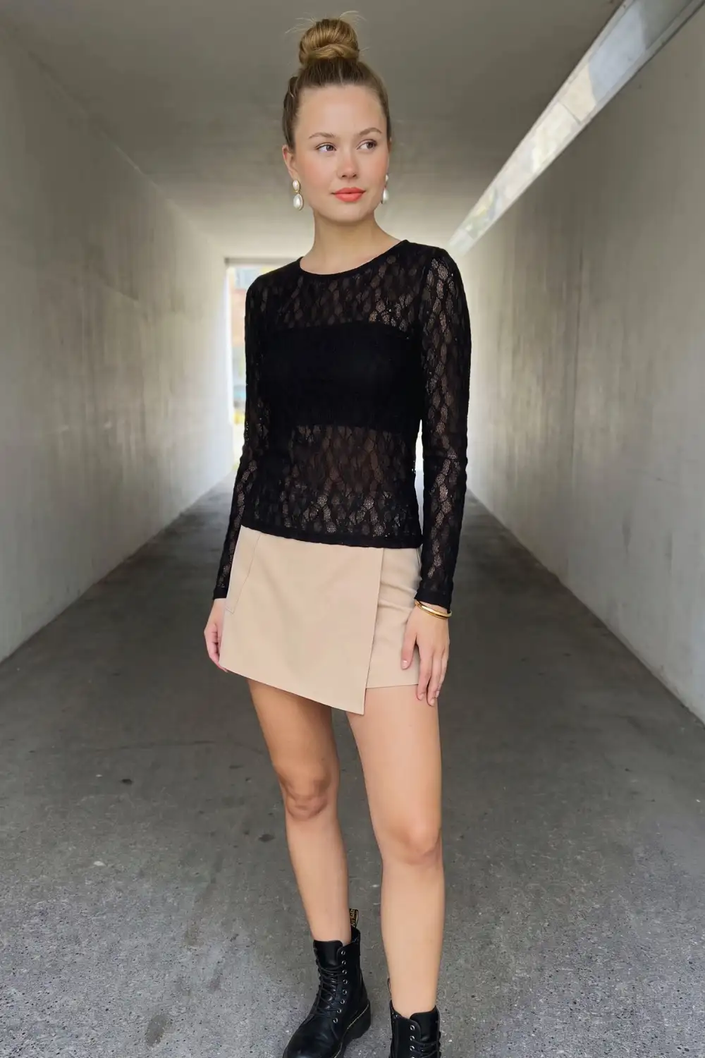 Woman in black sheer lace long sleeve top with beige asymmetric wrap mini skirt and black combat boots