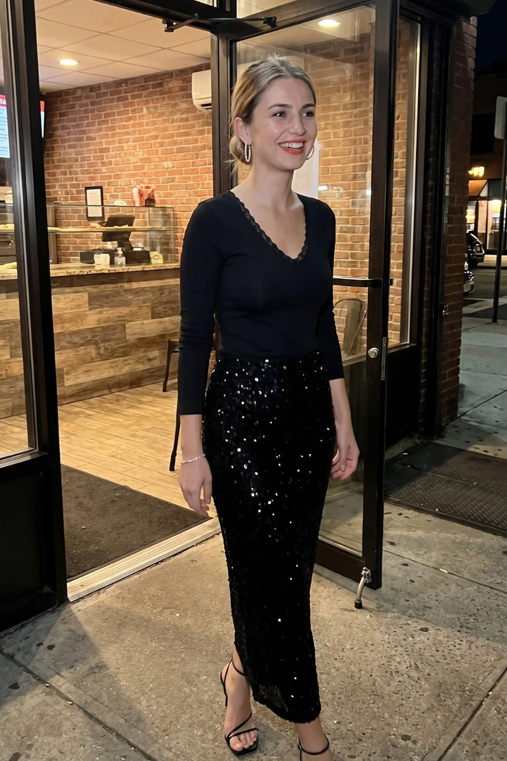 Woman in black lace trim v neck long sleeve top with black sequin maxi skirt and black strappy heels