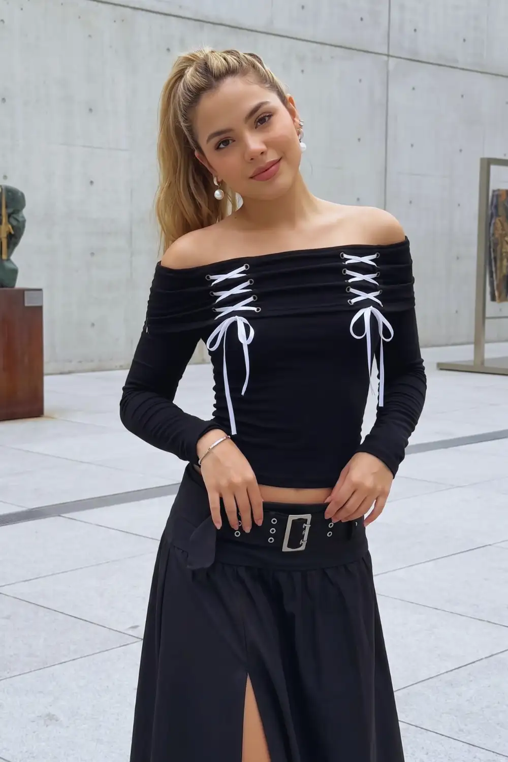 Woman in black off shoulder double lace up ribbon crop top with black belted slit midi skirt