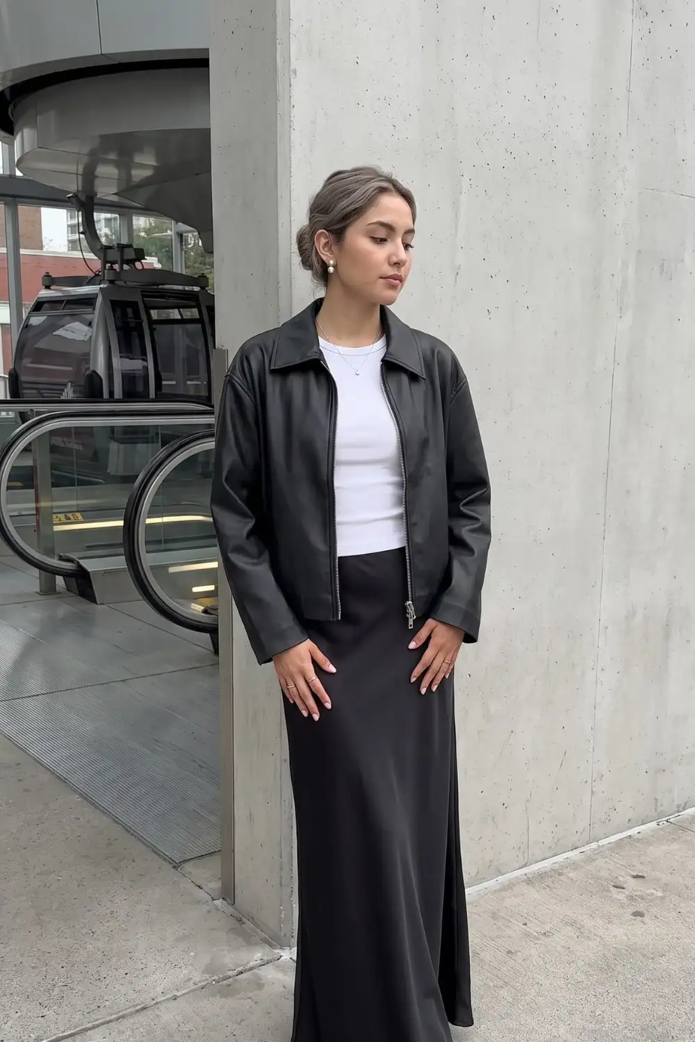 Woman in black oversized faux leather jacket with white ribbed crop top and black satin maxi skirt
