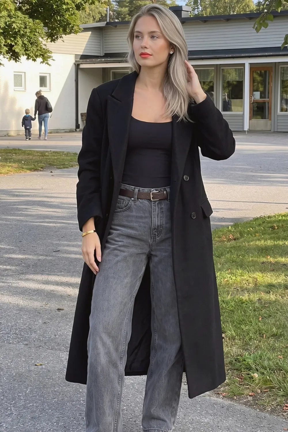 Woman in black long wool coat with black square neck bodysuit and grey belted wide leg jeans