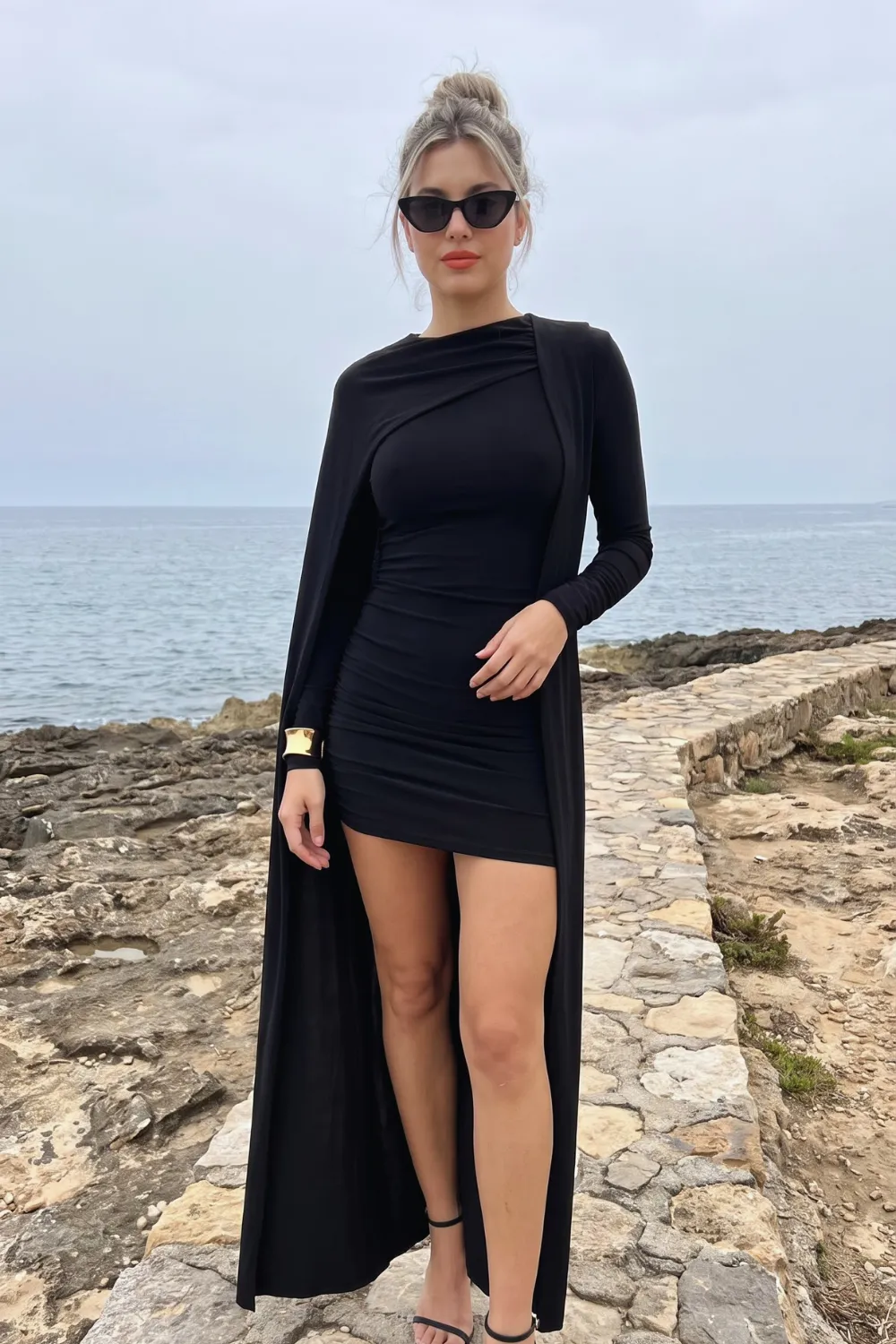 Woman in black ruched long sleeve mini dress with attached floor length cape