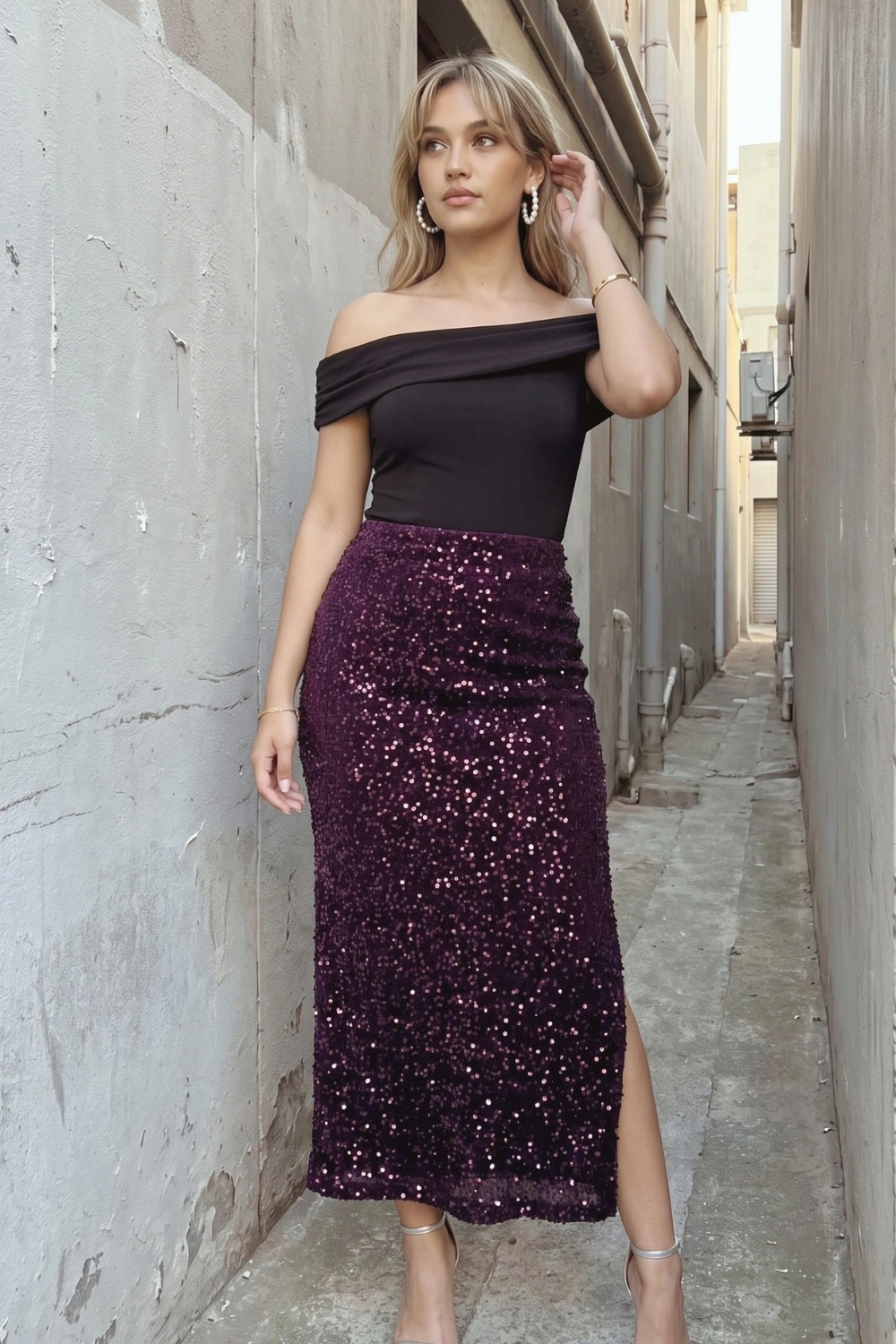 Woman in black off shoulder fitted top with deep purple sequin midi skirt with slit and silver heels