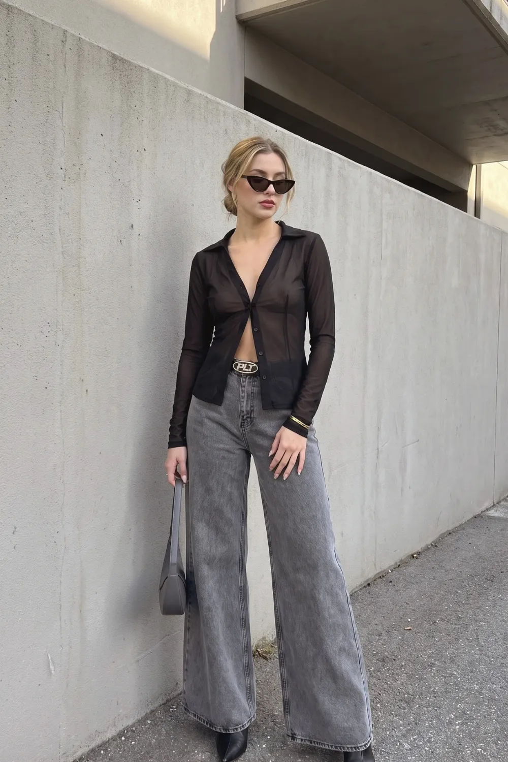 Woman in black sheer mesh button down shirt with grey acid wash wide leg jeans and black belt