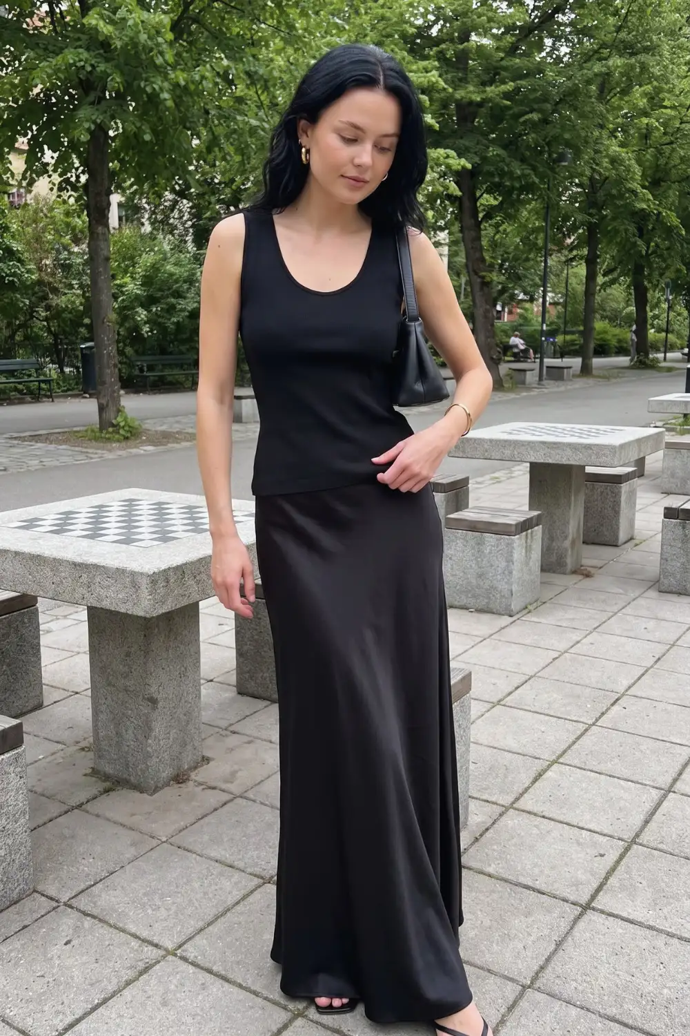 Woman in black scoop neck tank top with black satin bias cut maxi skirt and black flat sandals