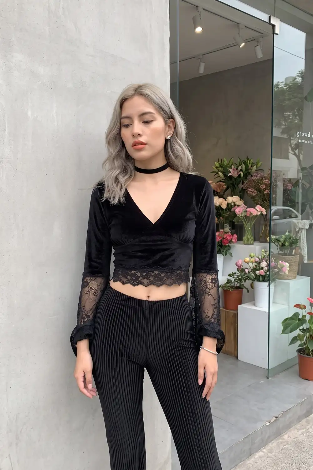 Woman in black velvet deep V lace trim wrap crop top with black pleated wide leg trousers