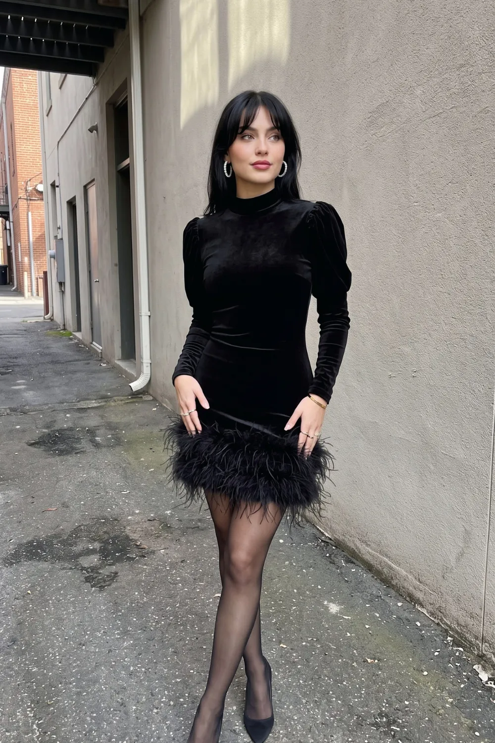 Woman in black velvet puff shoulder mock neck feather hem mini dress with sheer black tights
