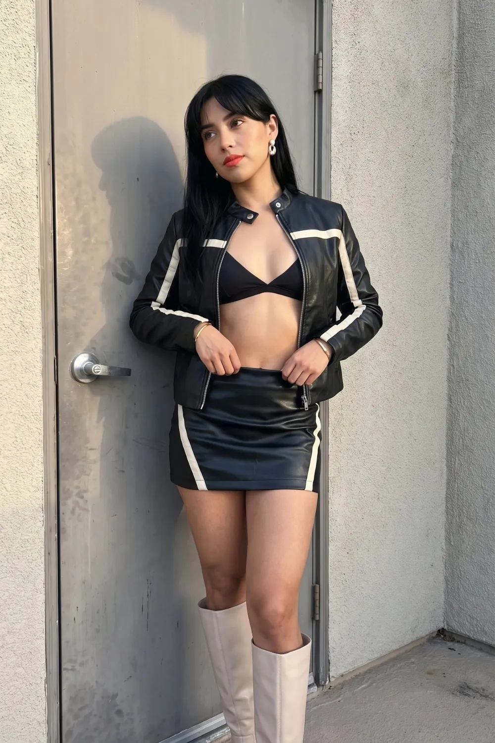 Woman in black white stripe leather moto jacket with black bikini top and matching mini skirt and white knee high boots