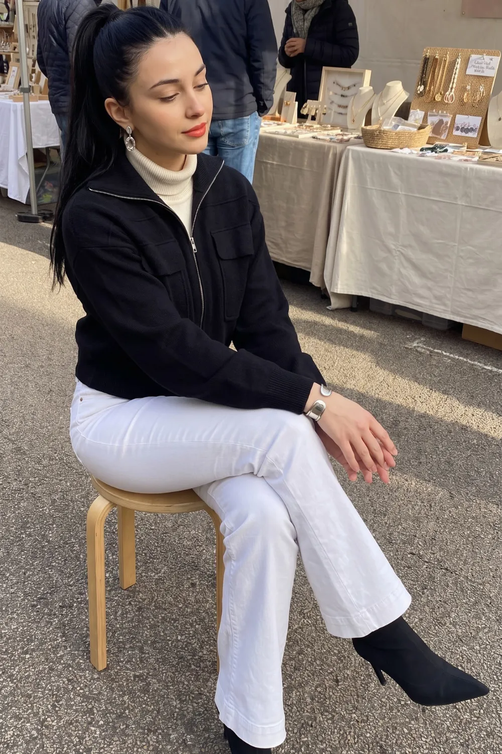 Woman in black zip knit jacket with cream turtleneck and white wide leg jeans