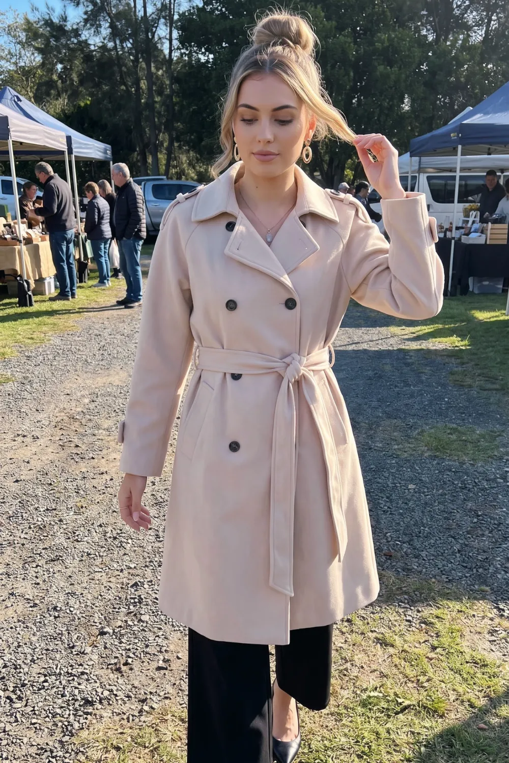 Woman in blush pink belted trench coat with black wide leg trousers and black heels