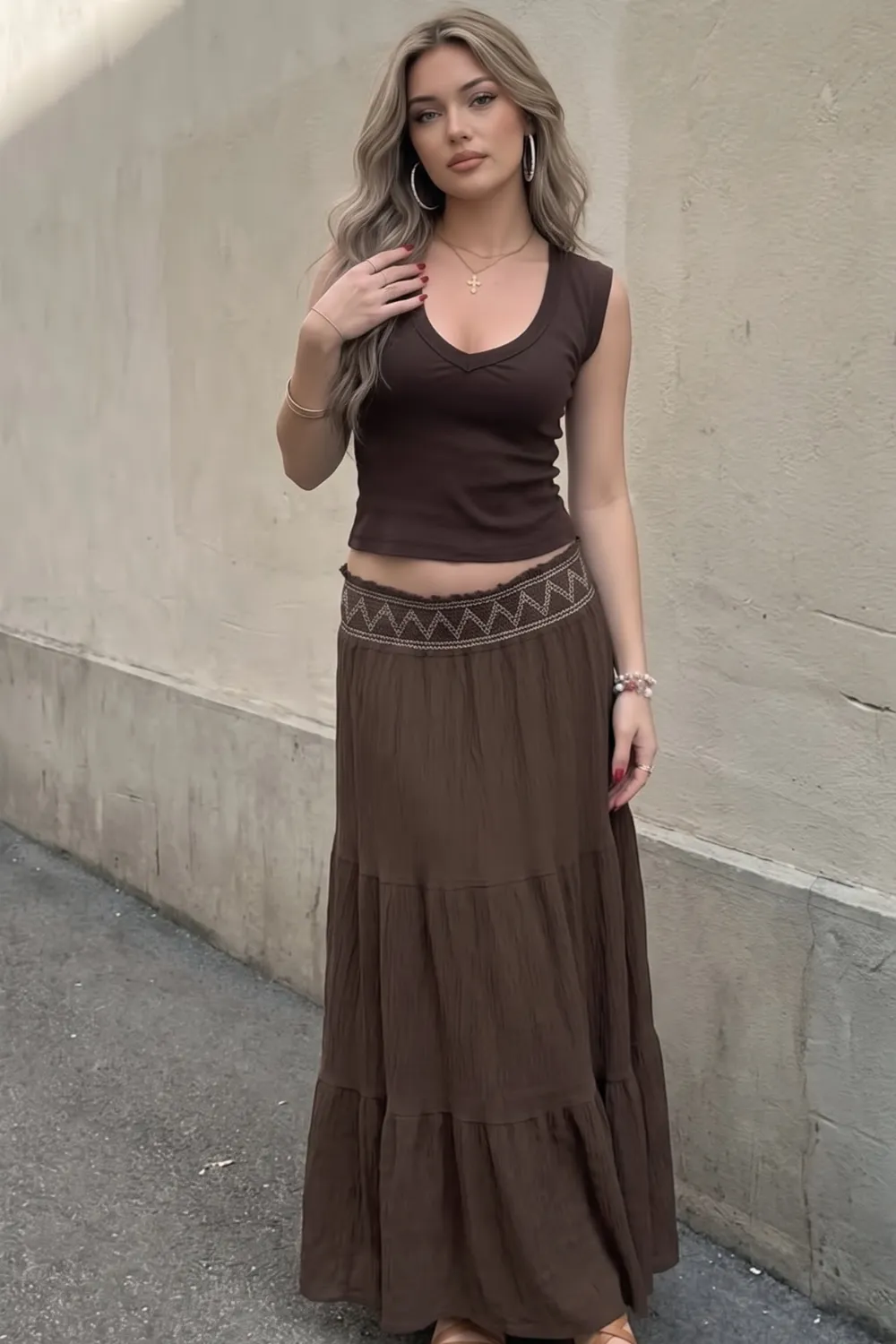 Woman in dark brown v neck sleeveless crop top and brown embroidered waistband tiered maxi skirt