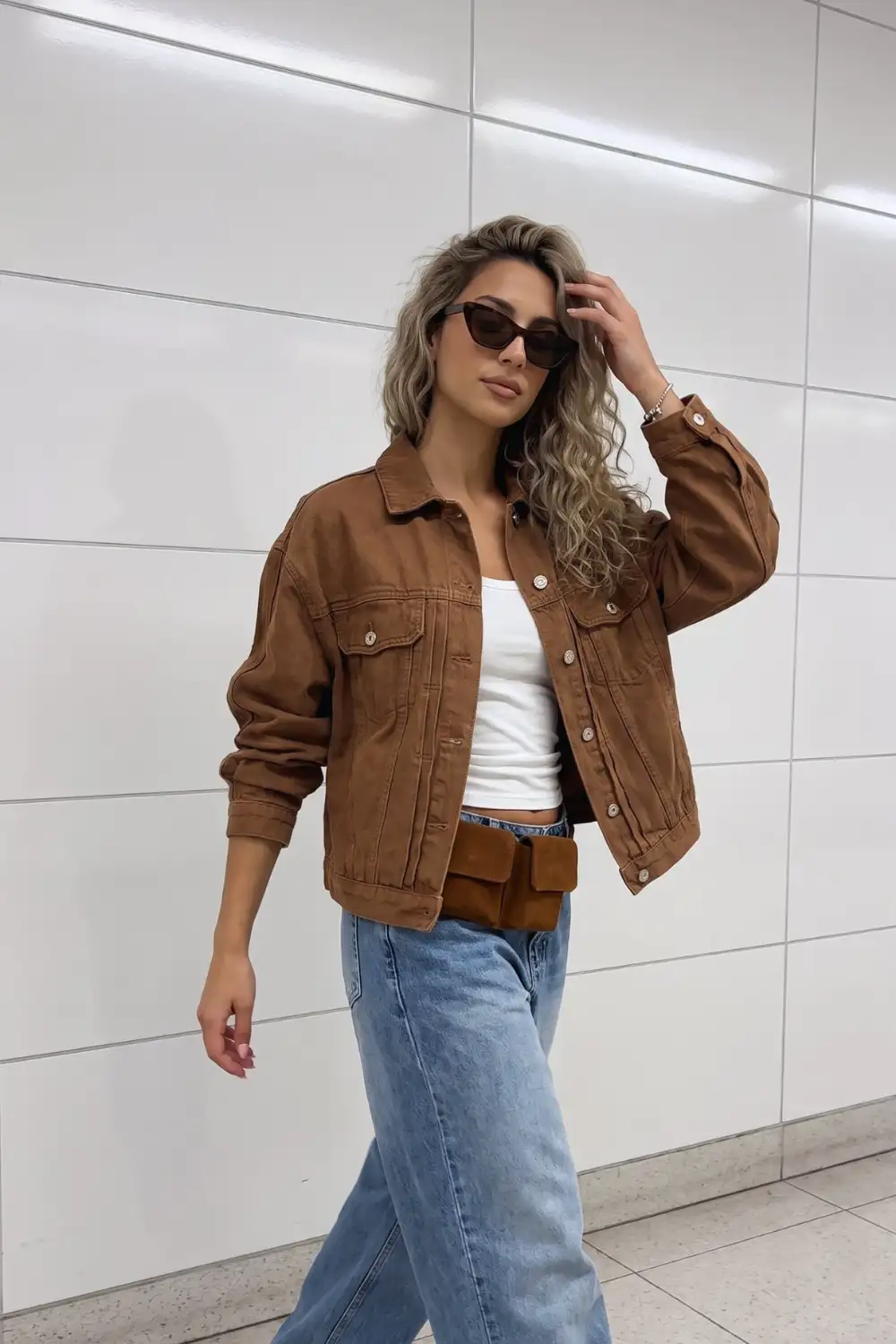Woman in tan brown oversized denim jacket with white crop top and light blue wide leg jeans