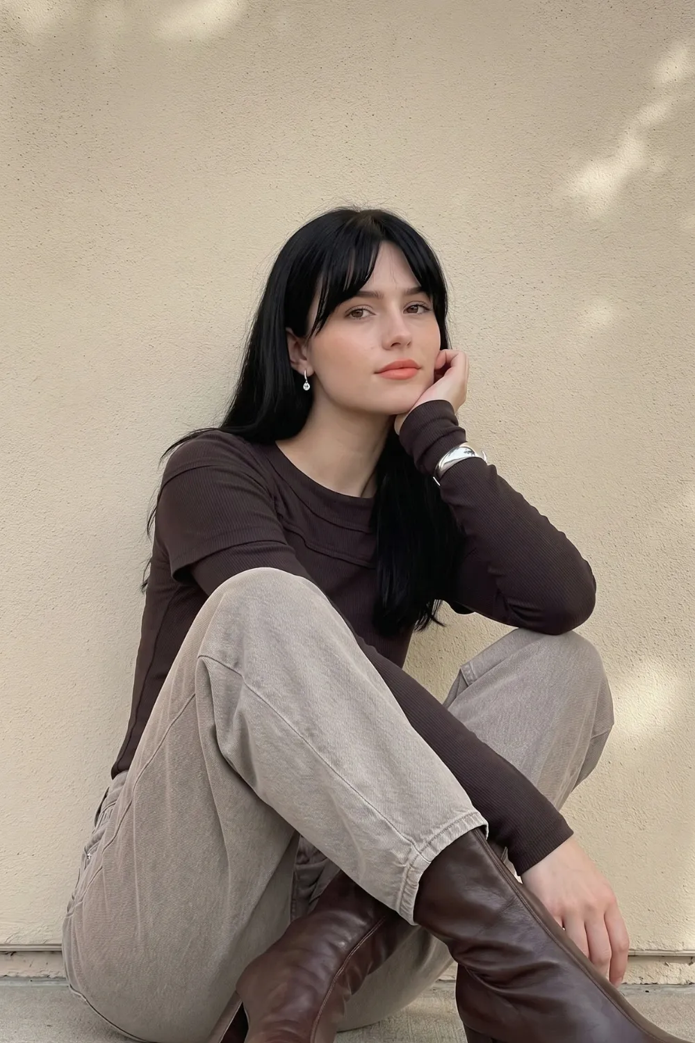 Woman in dark brown layered long sleeve top with light grey barrel jeans and brown leather boots