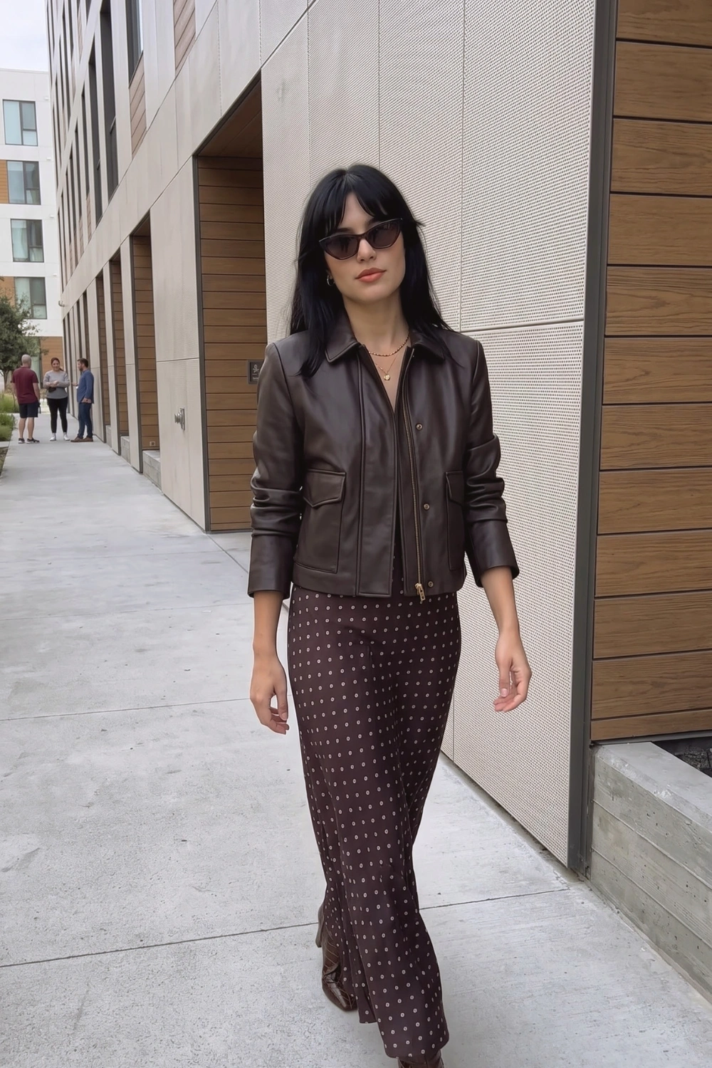 Woman in dark brown cropped leather jacket and dark brown polka dot satin midi skirt
