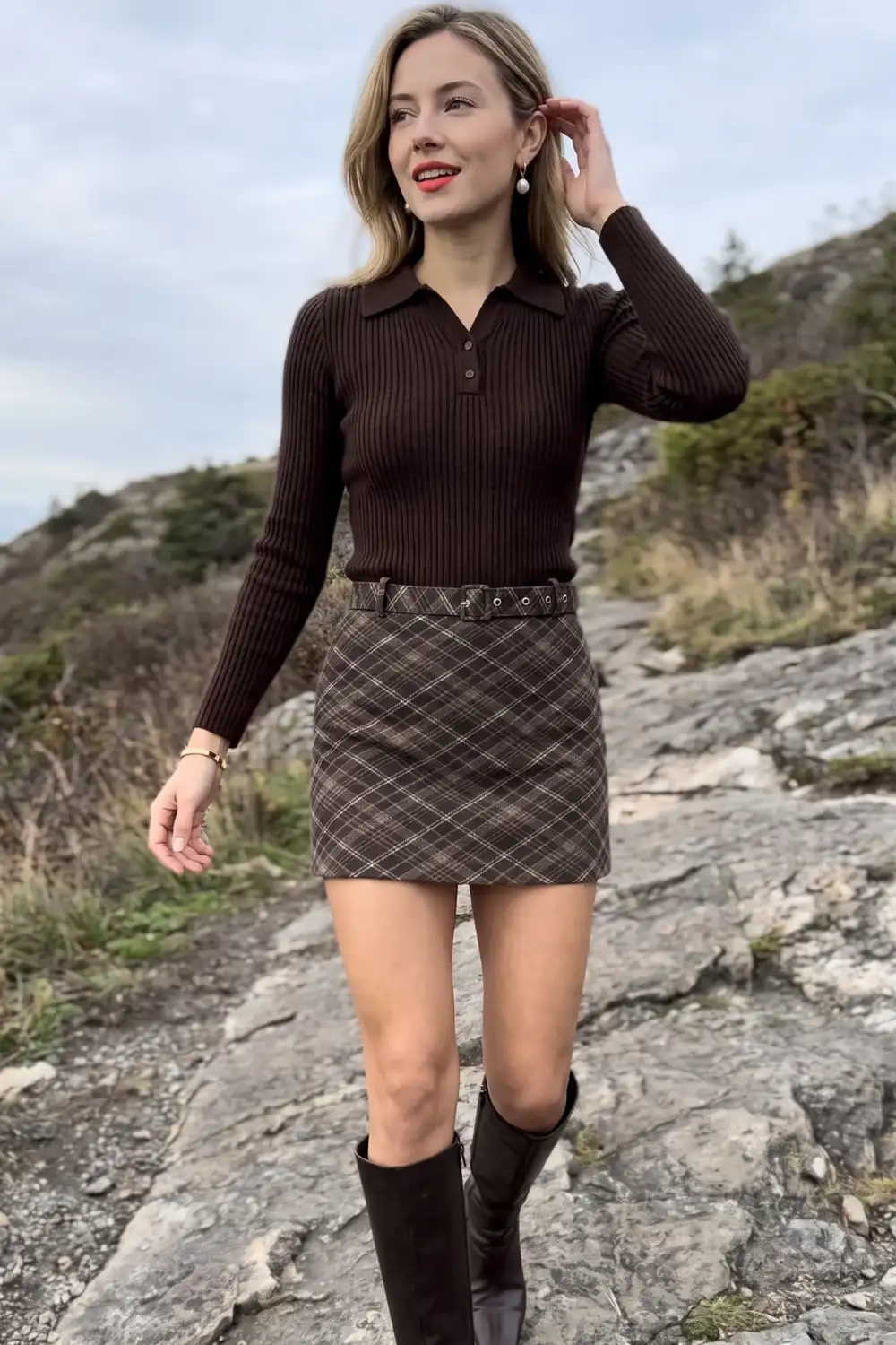 Woman in dark brown ribbed polo sweater with brown plaid mini skirt and knee high boots