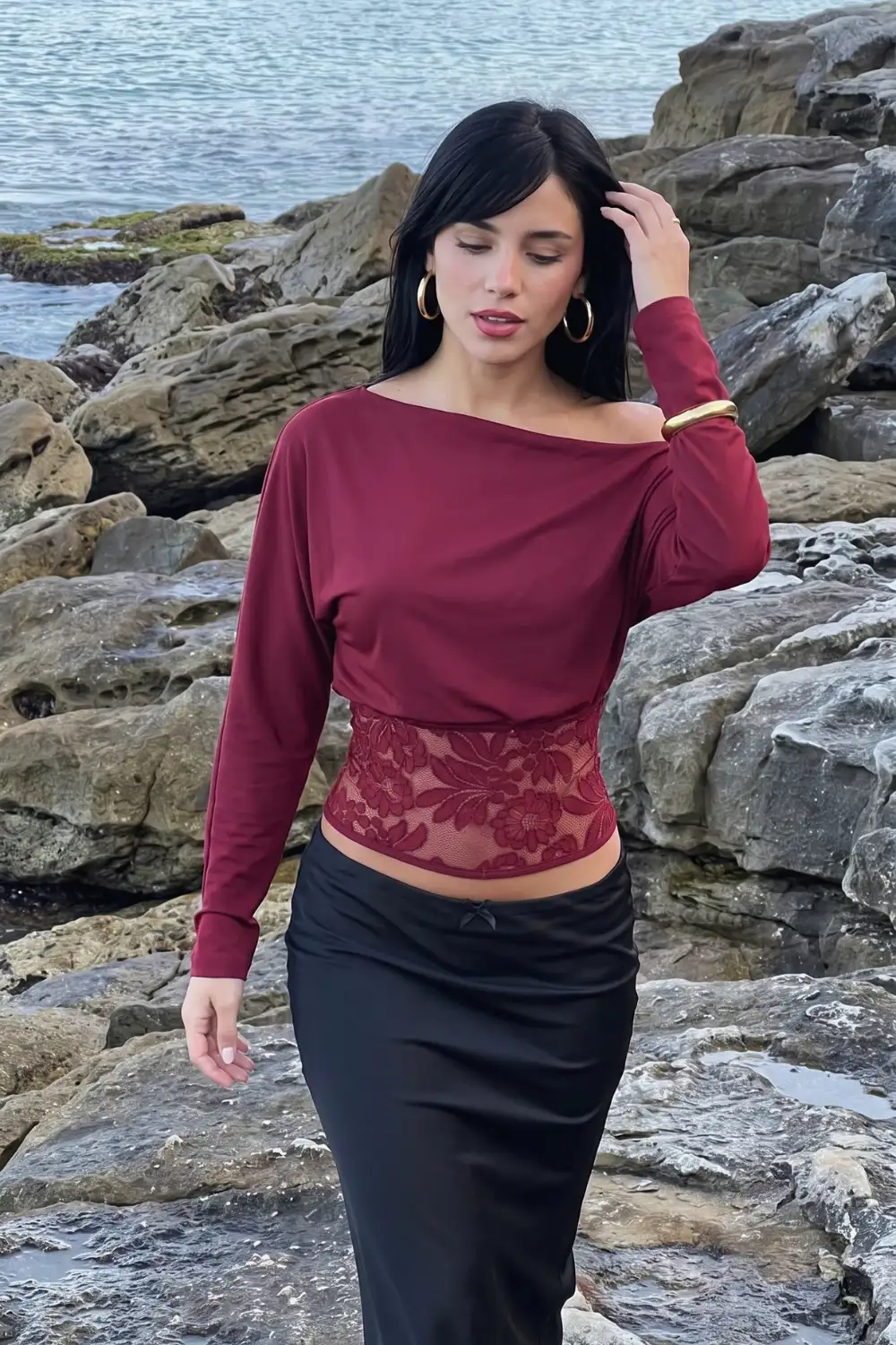 Woman in burgundy batwing off shoulder crop top with lace hem panel and black ruched bow midi skirt