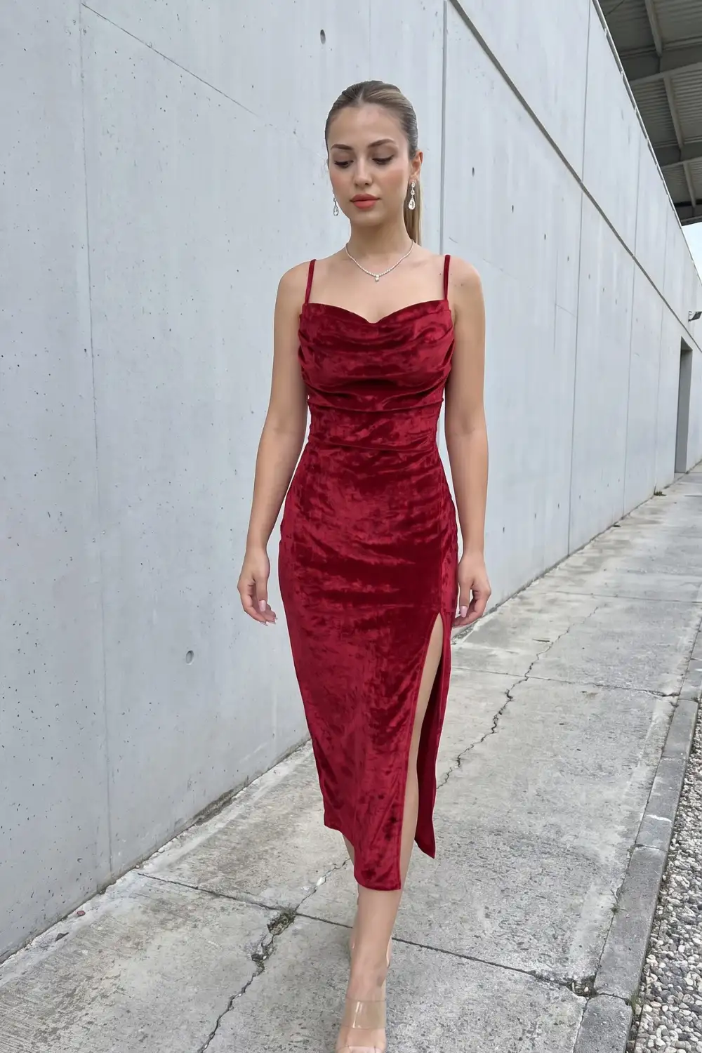Woman in burgundy crushed velvet spaghetti strap cowl neck ruched midi dress with side slit