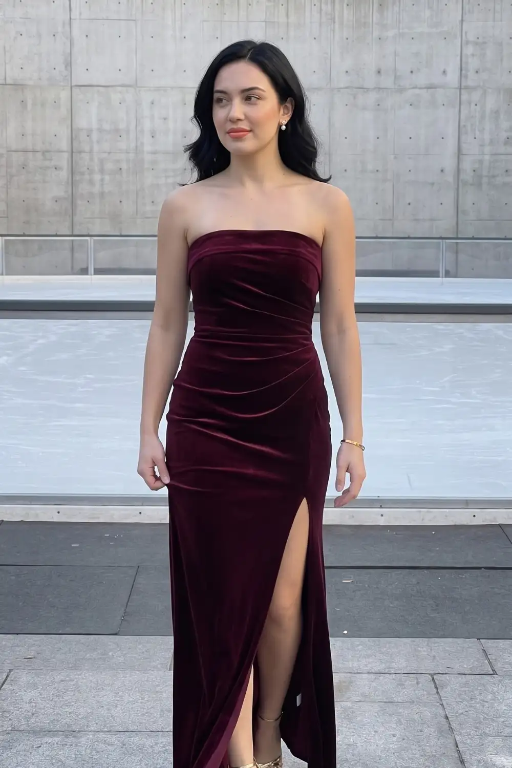 Woman in burgundy velvet strapless ruched fitted maxi dress with side slit