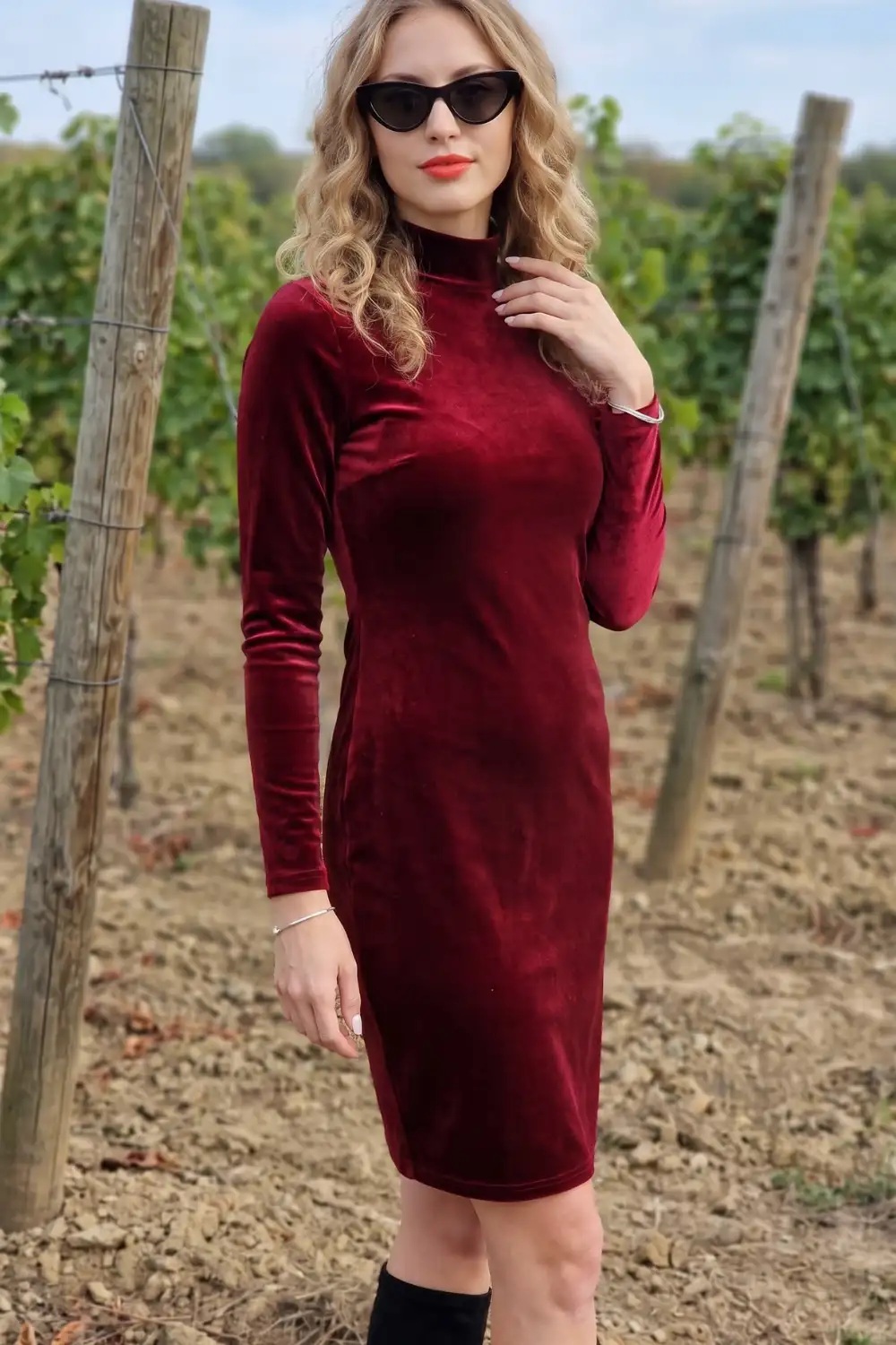 Woman in burgundy velvet mock neck long sleeve fitted midi dress with black knee high boots