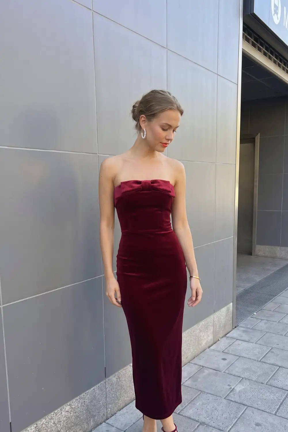 Woman in burgundy velvet strapless bow detail fitted midi dress