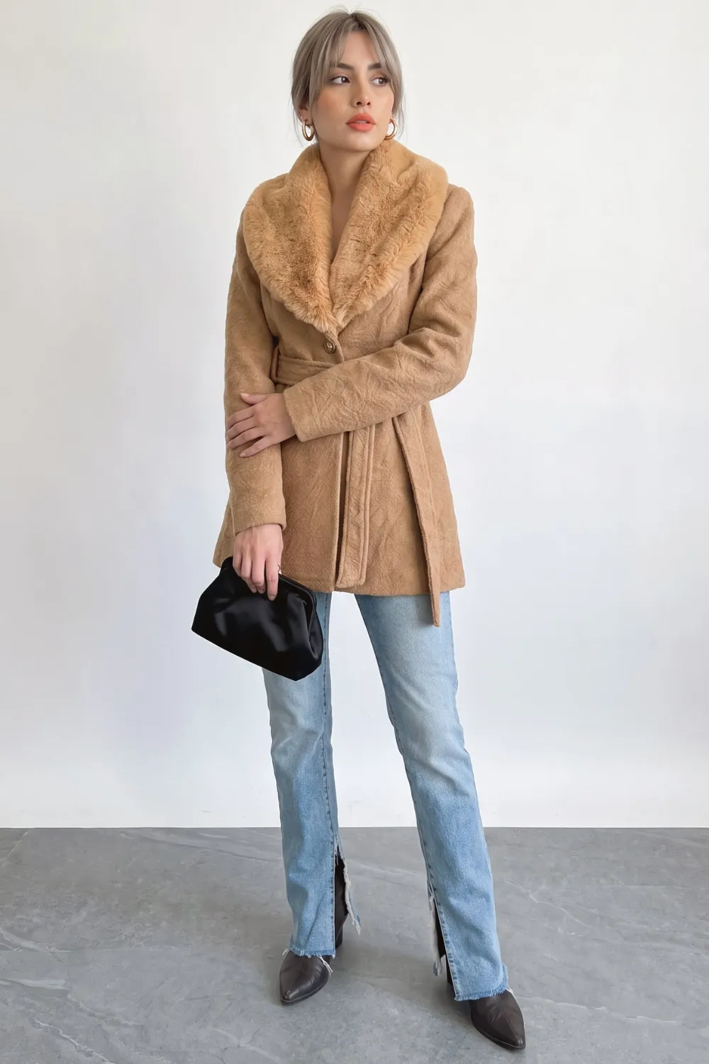 Woman in camel belted wool coat with faux fur lapel collar and light blue straight jeans