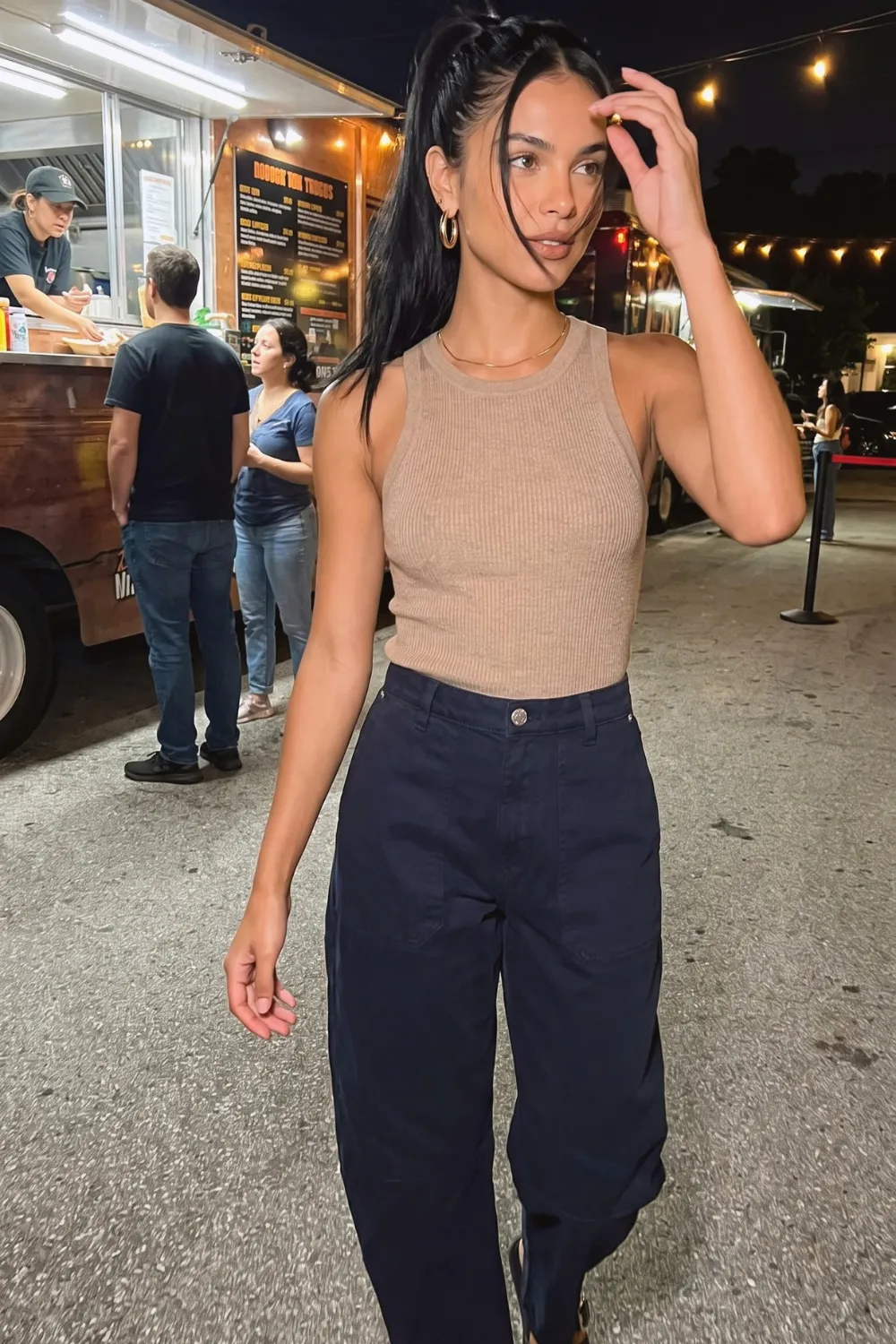 Woman in camel ribbed racerback tank top with navy blue barrel jeans