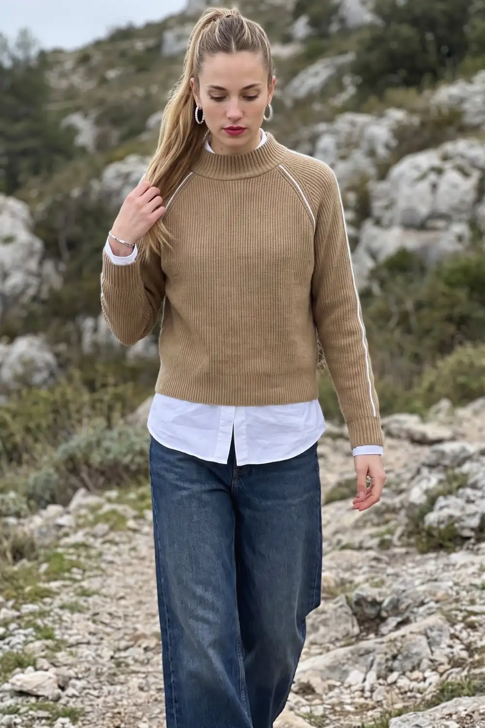 Woman in camel ribbed sweater layered over white shirt with dark wide leg jeans