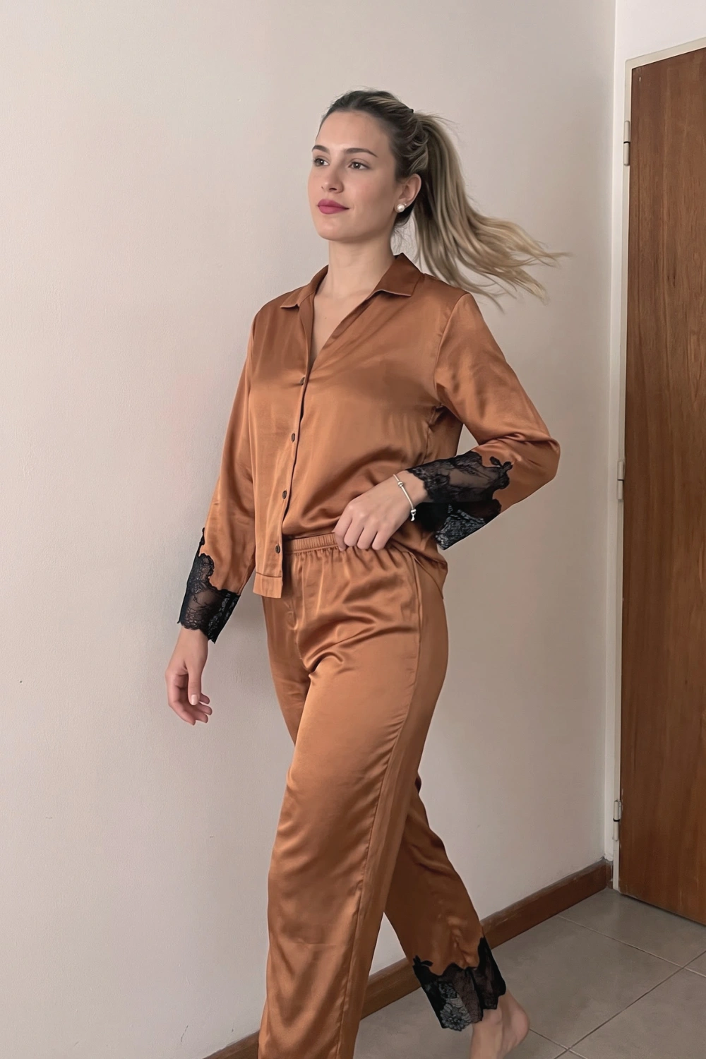 Woman in copper rust brown satin long sleeve button down shirt with black lace cuff trim and wide leg pants pajama set
