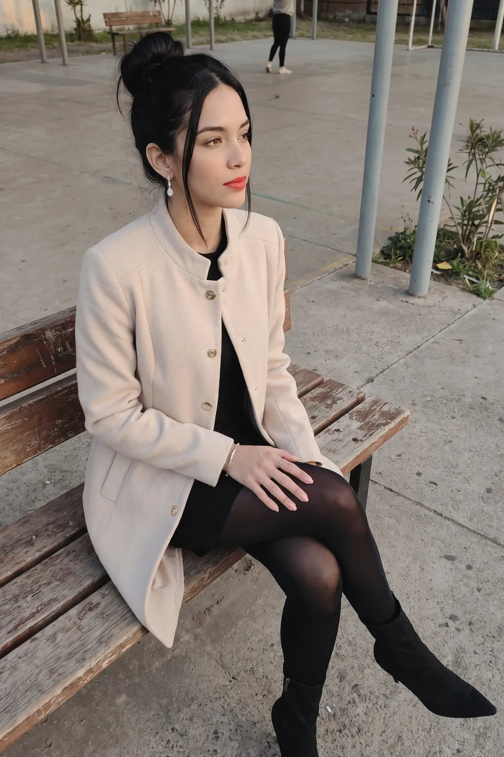 Woman in cream gold button blazer coat with black dress and black tights and pointed boots