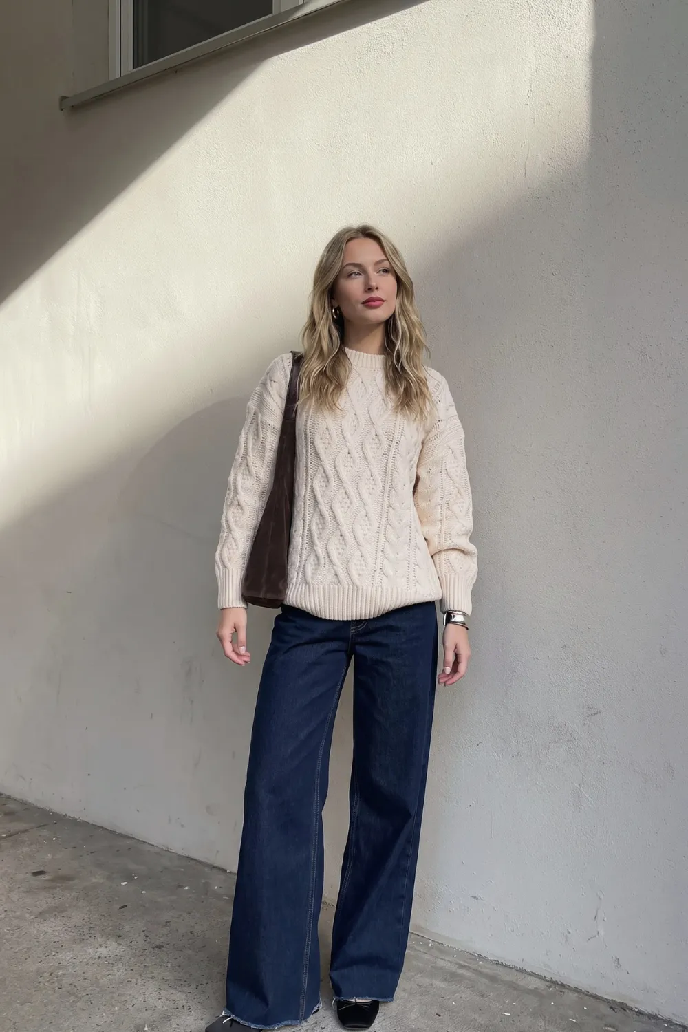 Woman in cream cable knit sweater with dark blue wide leg jeans