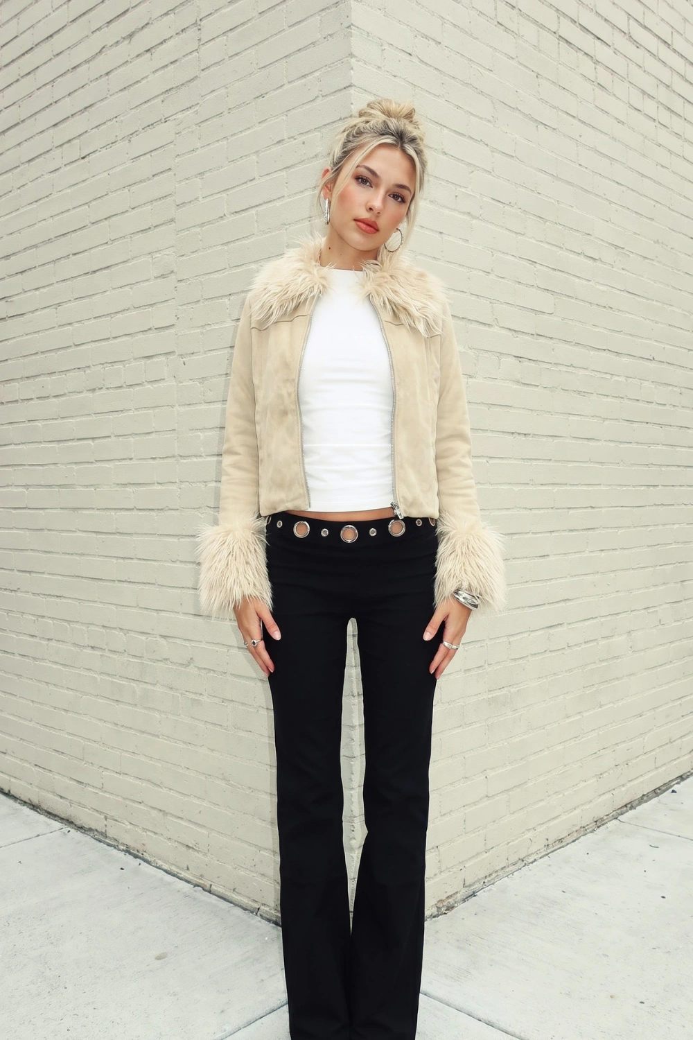 Woman in cream suede faux fur collar jacket with white crop top and black grommet low rise flare jeans