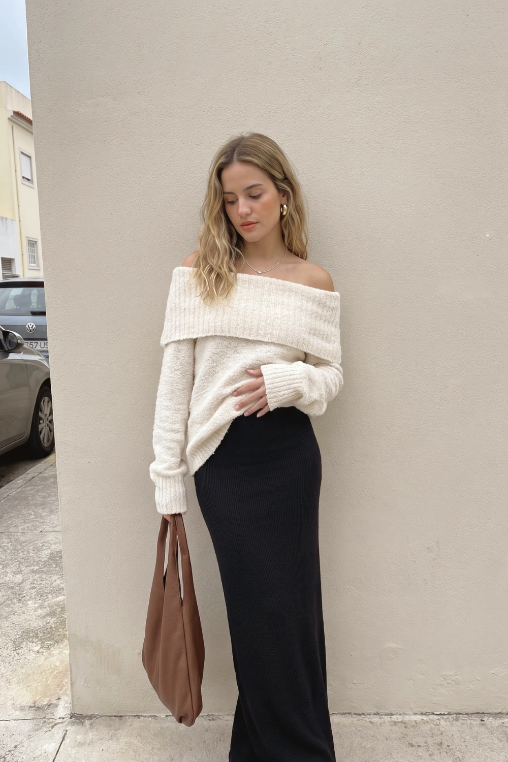 Woman in cream off shoulder oversized boucle knit sweater with black ribbed maxi skirt