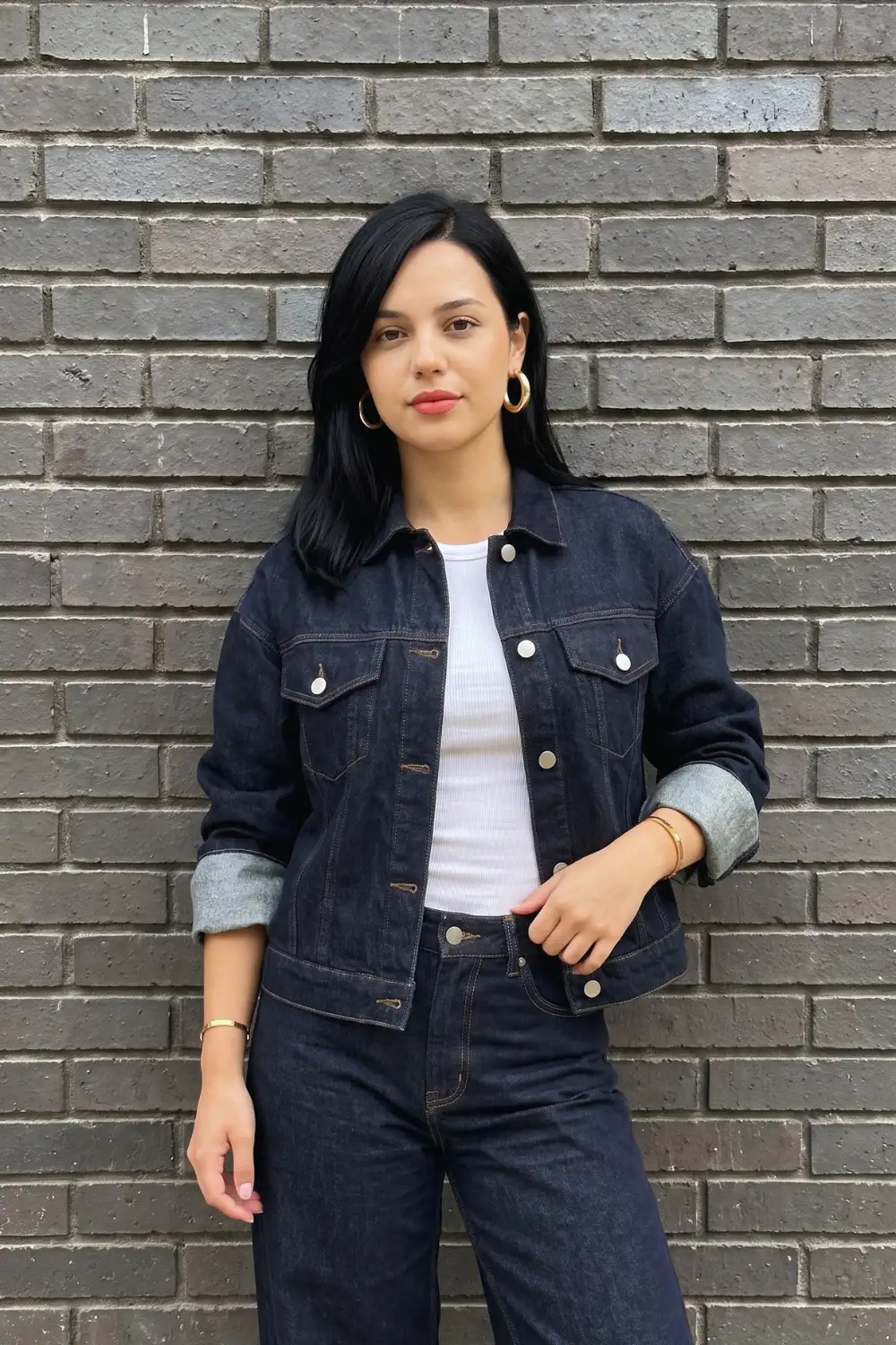 Woman in dark navy classic denim trucker jacket with white ribbed top and matching dark jeans