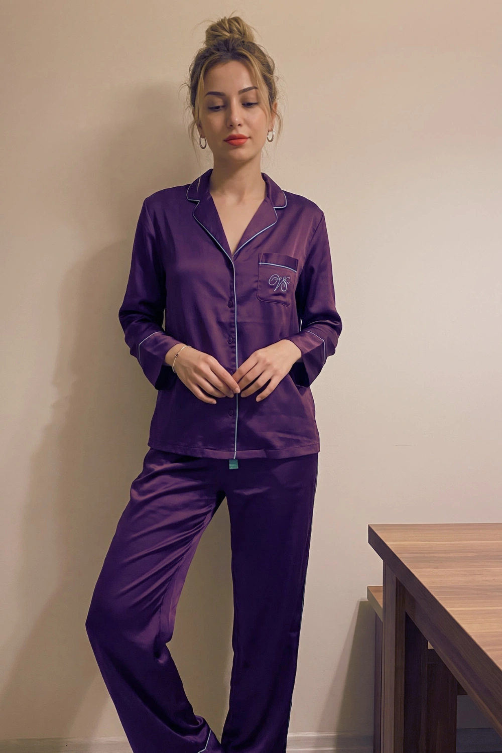 Woman in deep purple satin long sleeve button down shirt with white piping trim and wide leg pants pajama set
