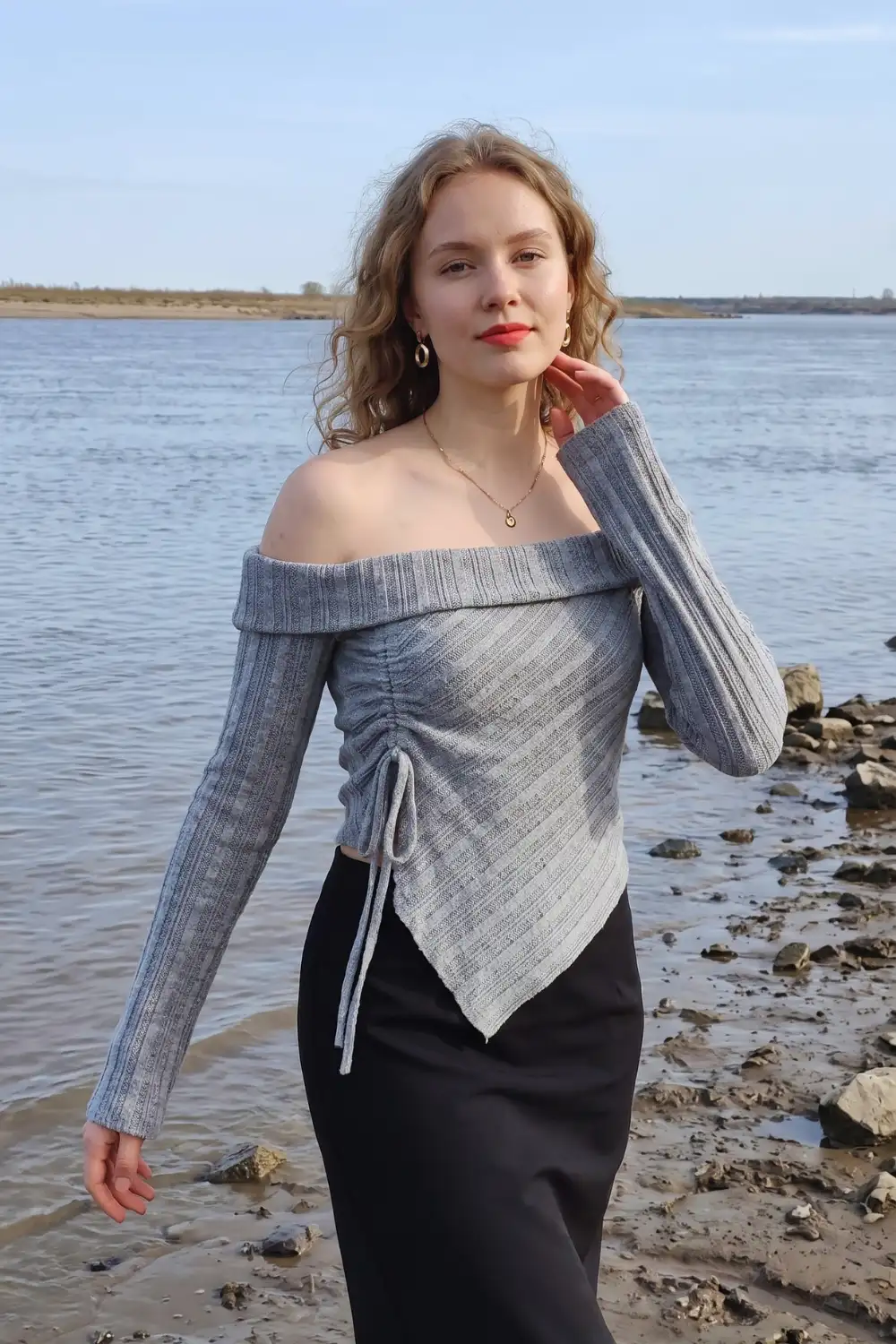 Woman in grey blue off shoulder ruched asymmetric knit top with black satin fitted midi skirt