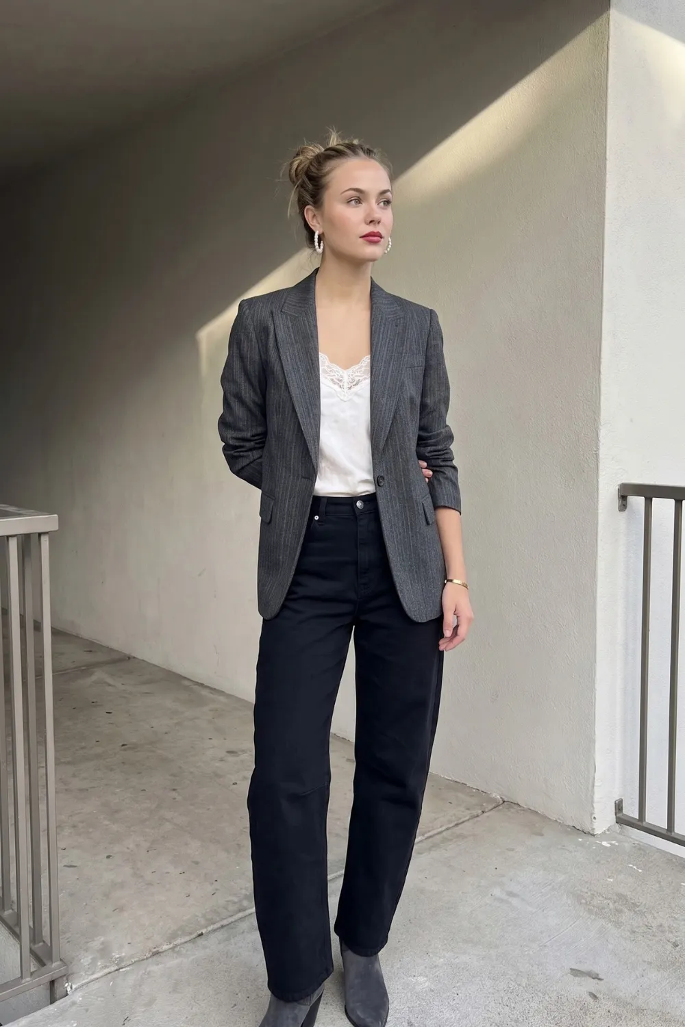 Woman in grey pinstripe blazer with white lace cami and black barrel jeans