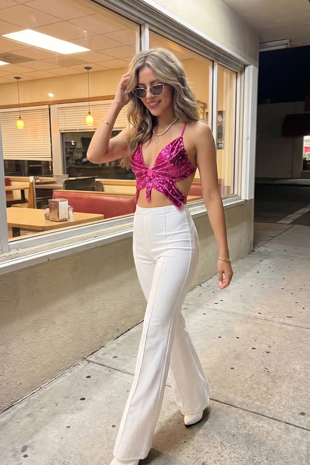Woman in hot pink sequin butterfly tie front crop top with white high waist flare trousers