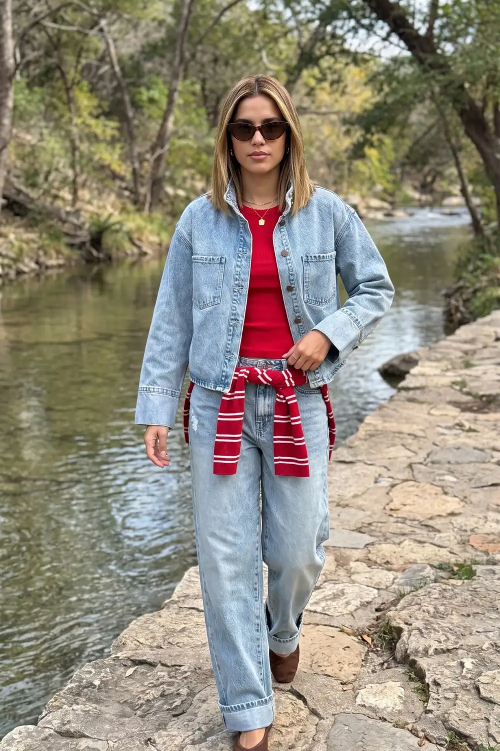 Woman in light blue denim jacket with red crop top wide leg jeans and striped sweater tied at waist