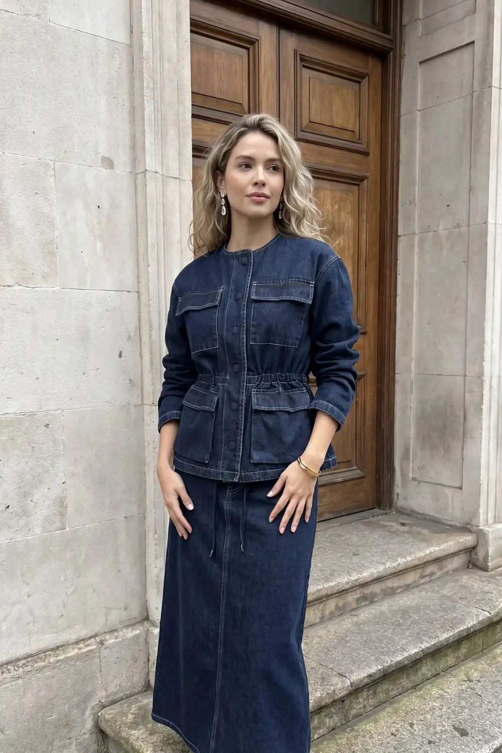 Woman in dark navy collarless denim utility jacket with drawstring waist and matching maxi skirt